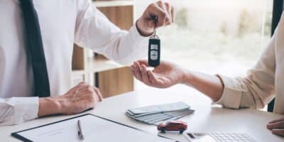 A financing specialist hands over a keys to a new car purchased by a new owner.
