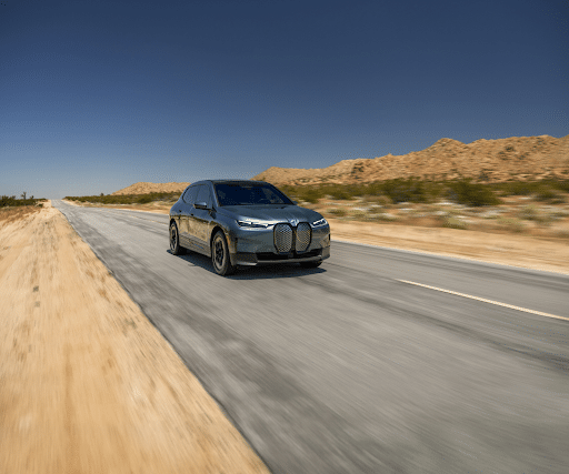 A BMW driving down an empty sandy road.