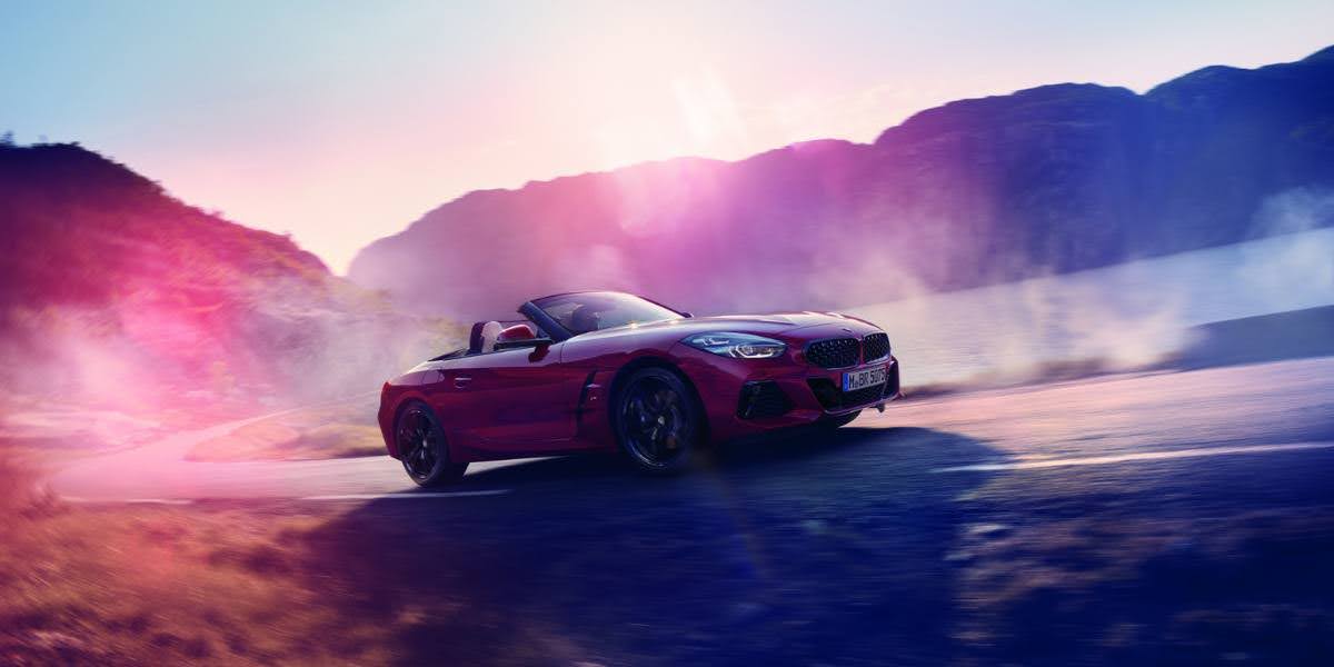 A dynamic shot of a red BMW Z4 M40i convertible speeding along a scenic mountain road, embodying BMW's driving excitement and precision.