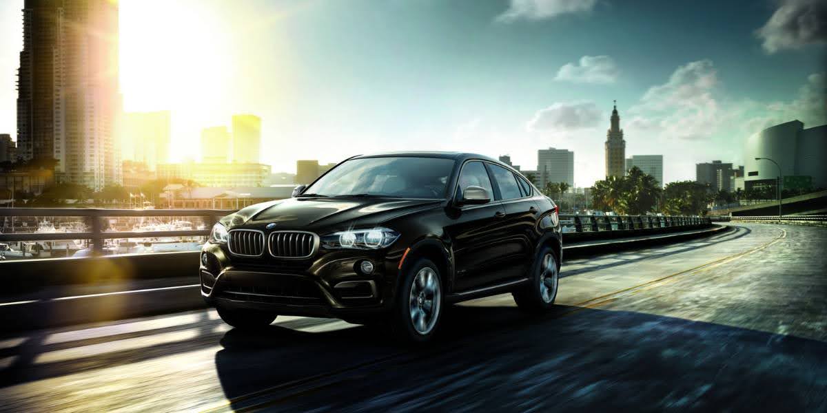 A sleek black BMW X6 cruising through a city skyline, highlighting its dynamic design and urban appeal