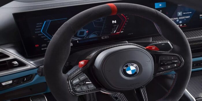 Close-up of the 2025 BMW M4 Convertible steering wheel with advanced controls, red M mode buttons, and a high-tech digital instrument cluster.