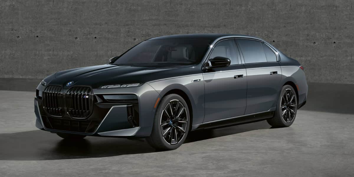 A sleek black and gray 2025 BMW i7 parked in an industrial setting, showcasing its bold kidney grille, aerodynamic body, and futuristic headlights.