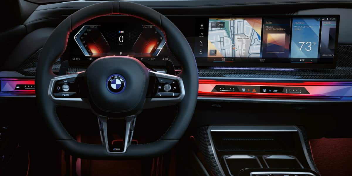 The driver’s cockpit of the 2025 BMW i7, featuring a digital curved display, illuminated dashboard, and a leather-wrapped steering wheel