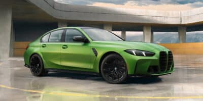 A vibrant green 2025 BMW M3 parked in a modern concrete setting, highlighting its bold grille, aerodynamic design, and black alloy wheels.