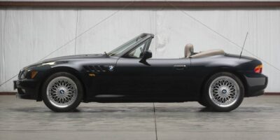 Side profile of a black bmw z3 convertible roadster with top down, parked indoors on a concrete floor.