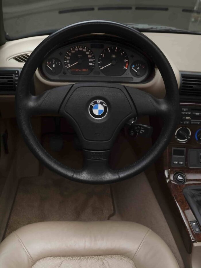 Driver’s view of a bmw z3 interior with black steering wheel, analog gauges, and beige cabin materials.