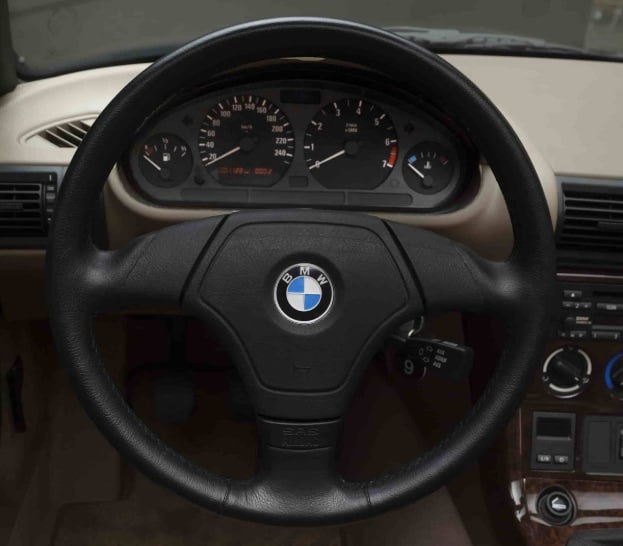 Driver’s view of a bmw z3 interior with black steering wheel, analog gauges, and beige cabin materials.