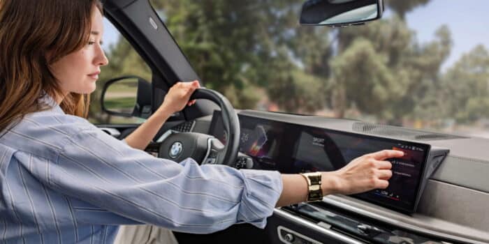 Driver using BMW Highway Assistant touchscreen feature while cruising, showing hands-free driving technology and safety focus inside BMW cabin.
