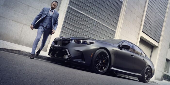 Man in suit walking near a matte black BMW M5 parked on a city street, highlighting the sporty luxury design of the M5 BMW.