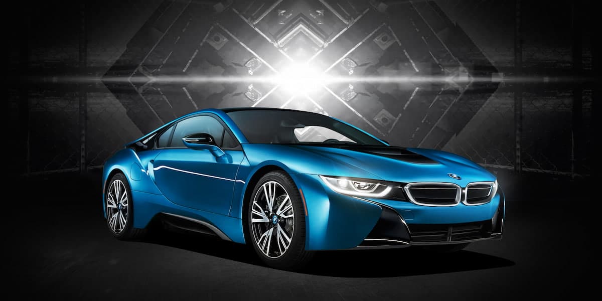 Blue BMW i8 plug-in hybrid sports car in a studio setting with dramatic backlight, front three-quarter view.