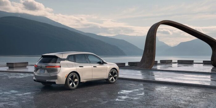BMW battery preconditioning shown with a BMW electric vehicle parked near a modern sculpture by a lake, illustrating advanced EV technology.