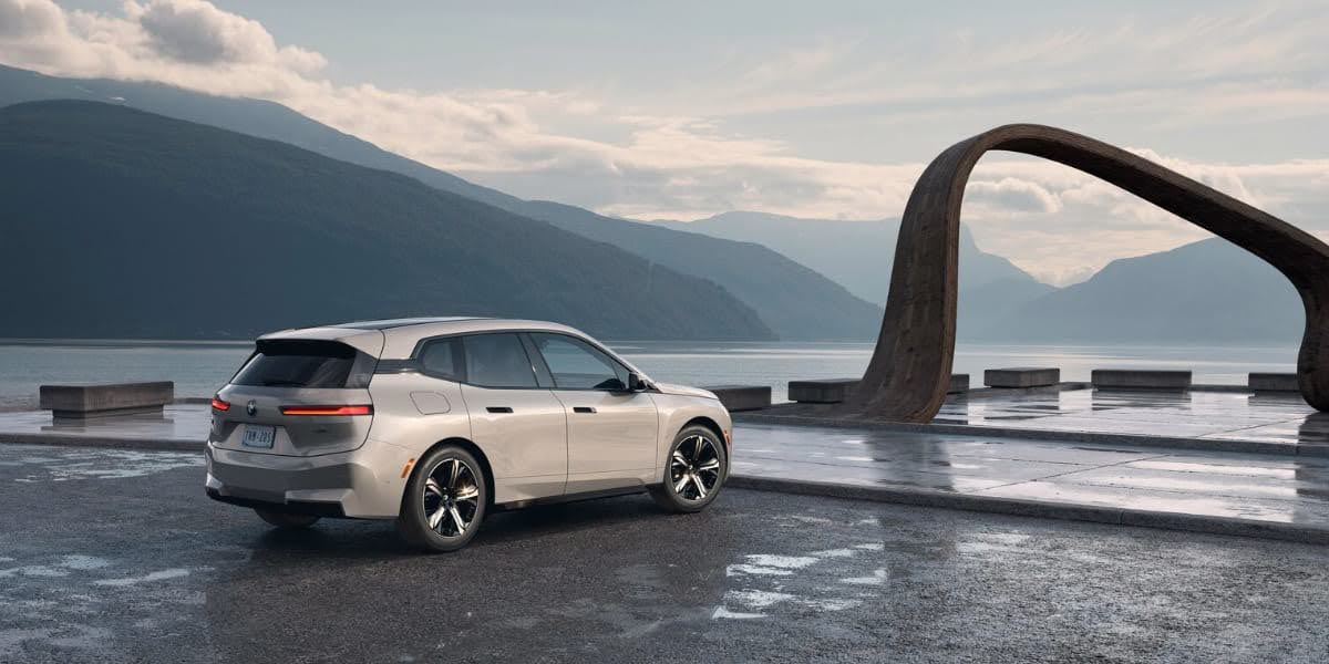 BMW battery preconditioning shown with a BMW electric vehicle parked near a modern sculpture by a lake, illustrating advanced EV technology.