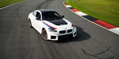 Front three quarter view of a white 2026 BMW M2 performance coupe on a racetrack with M stripes and black hood detail